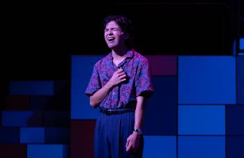 A photo from a performance of "Company," depicting an actor mid song. His face is filled with sorrow as his hand covers his heart.