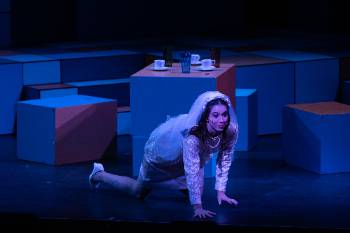 A photo from a performance of "Company," depicting a woman in a wedding dress and veil, crawling on her hands and knees.