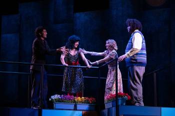 A photo from a performance of "Company," depicting a group of four actors conversating on a balcony.