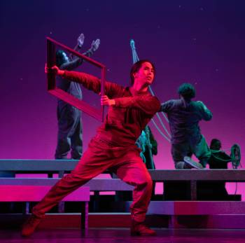 A photo depicting a performance of "Kingdom of Cards," depicting an actor posed with an empty photo frame in stark red and blue lighting.