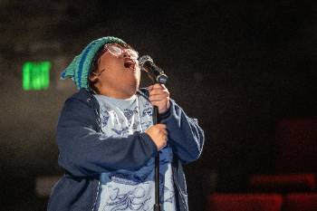 A photo depicting a performance of "Wolf Play," depicting an actor in the middle of yelling loudly into a microphone.