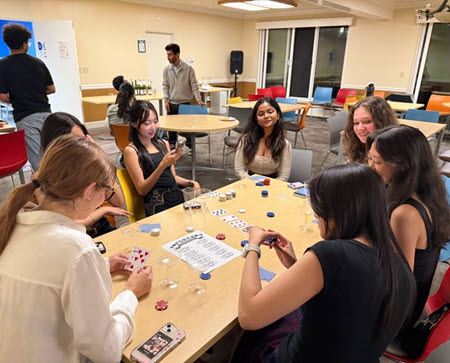 Students gathered around a table with cards and poker chips, watching as one player counts their chips for a play