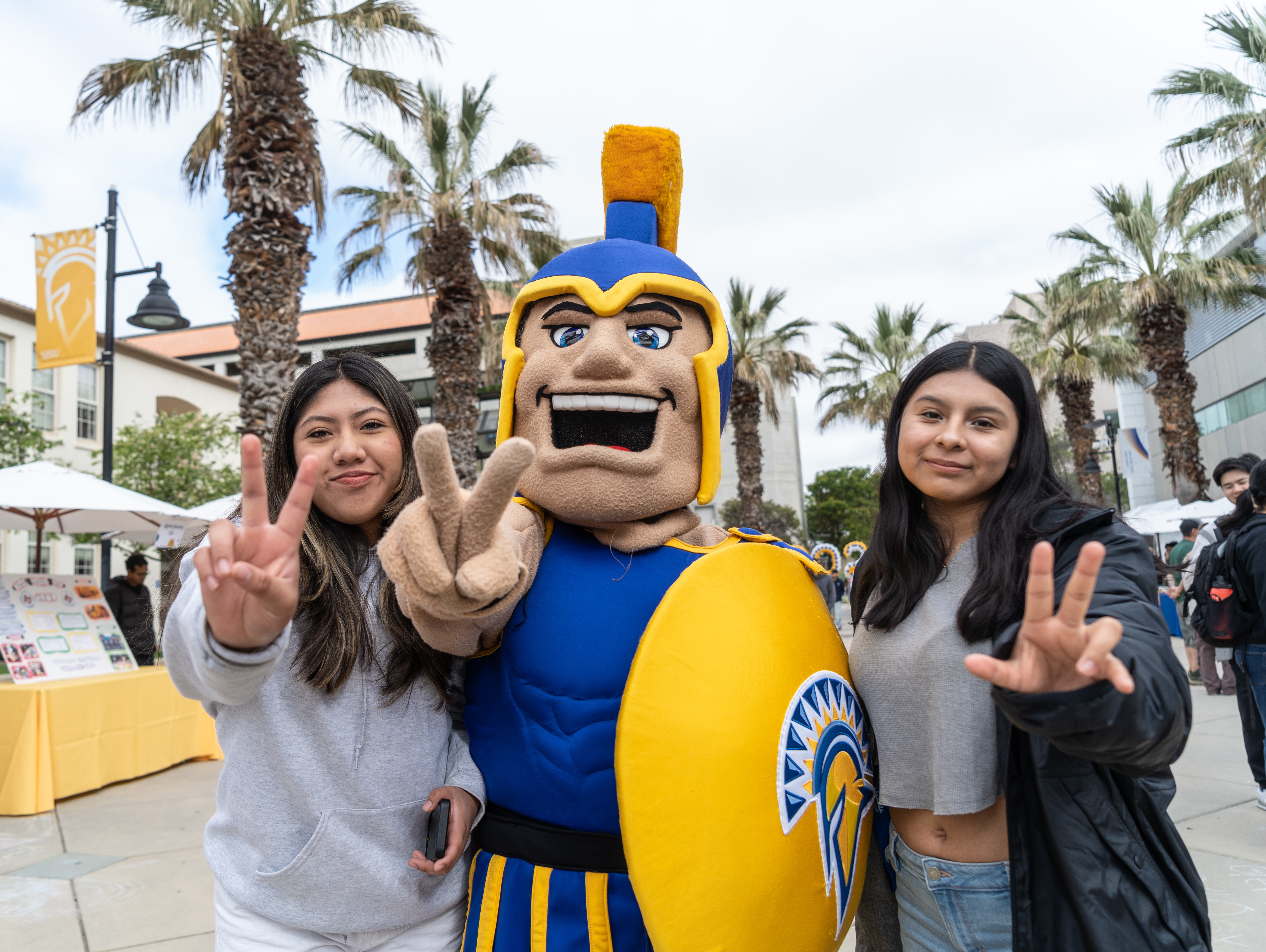 Two newly admitted students give the peace sign while posing alongside Sammy.