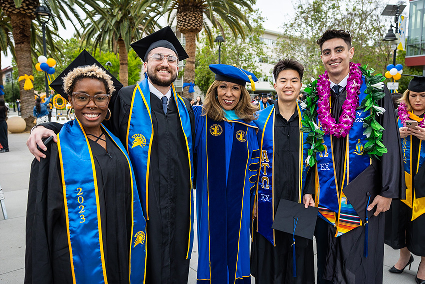 SJSU graduates posing with the university president at their graduation ceremony.